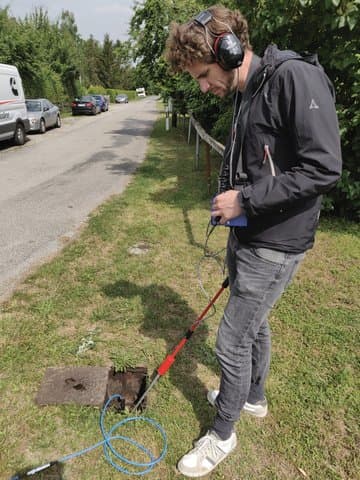 A field technician using an acoustic sensor rod to detect leaks on a water pipe